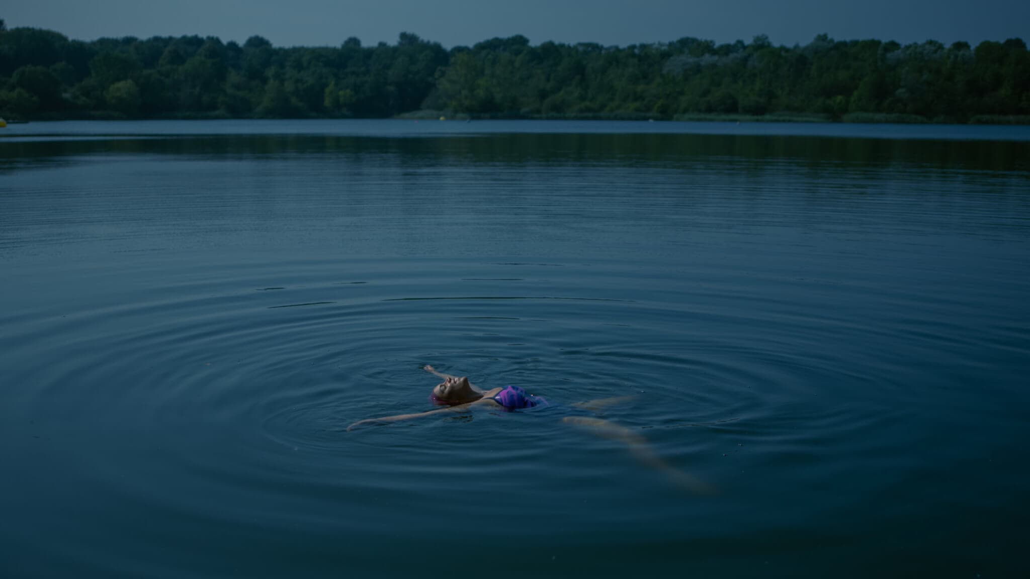 A Black woman floats alone in a deep blue body of water, in a film.